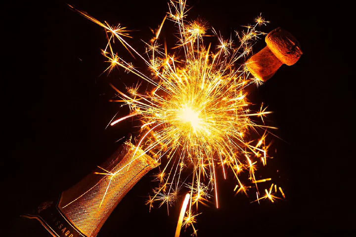 Uma garrafa de champagne sendo aberto mas entre a rolha e a garrafa tem o estouro de um fogo de artifício